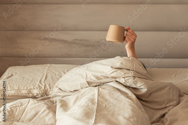 Obraz A hand holding a coffee mug emerging from a cozy bed.