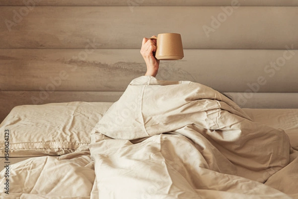Obraz A hand holding a coffee mug emerging from a cozy bed.
