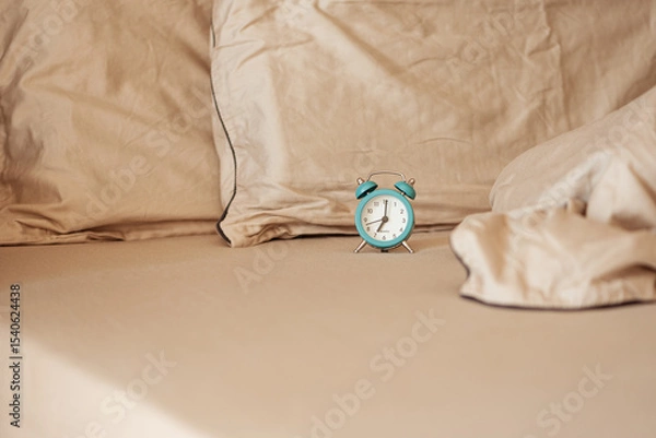 Obraz Alarm clock on an unmade bed in the morning light.