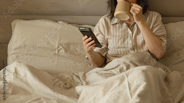 Obraz Woman drinking coffee and using phone in bed in the morning.