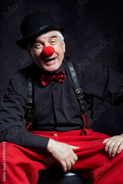 Fototapeta Portrait of a clown on dark background  with red clown nose and bowler hat on head.