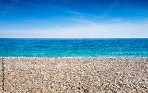 Obraz Pebble beach stretches along calm turquoise sea under bright blue sky. Sea and beach meet at clear horizon on sunny summer day. Peaceful coastal landscape without people or buildings