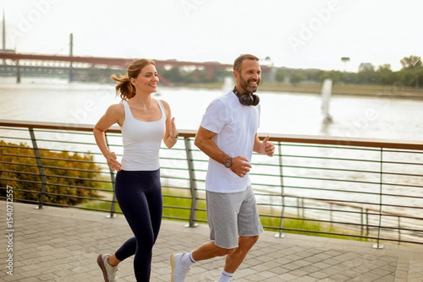 Obraz Couple enjoys a morning jog along the riverside pathway in a vibrant urban setting