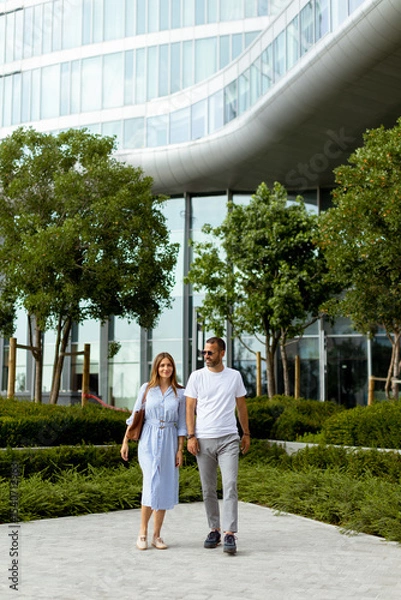 Obraz Couple strolls through lush green landscape near modern architecture on a sunny day