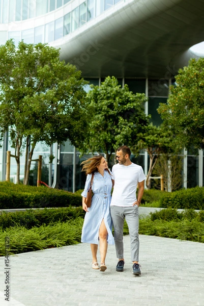 Obraz Couple enjoys a joyful stroll through a modern garden in the heart of the city on a sunny afternoon