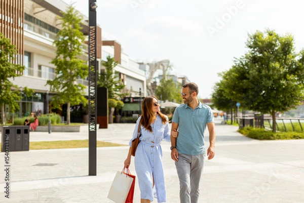 Obraz Couple enjoying a sunny day strolling through a vibrant shopping district with colorful storefronts and lush greenery
