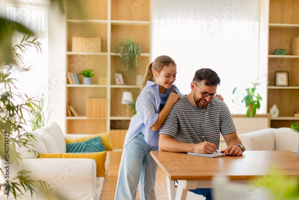 Obraz Joyful moments shared between a father and daughter while writing at home in a bright, cozy living room filled with greenery