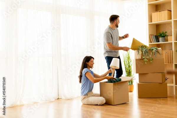 Obraz Couple unpacks boxes together in bright living room, creating a cozy new home full of warmth and excitement during the afternoon
