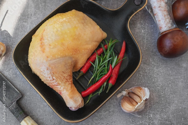 Fototapeta Raw chicken leg. A piece of fresh raw chicken leg with red chilli. displayed on a black stylish ceramic baking pan. Top view