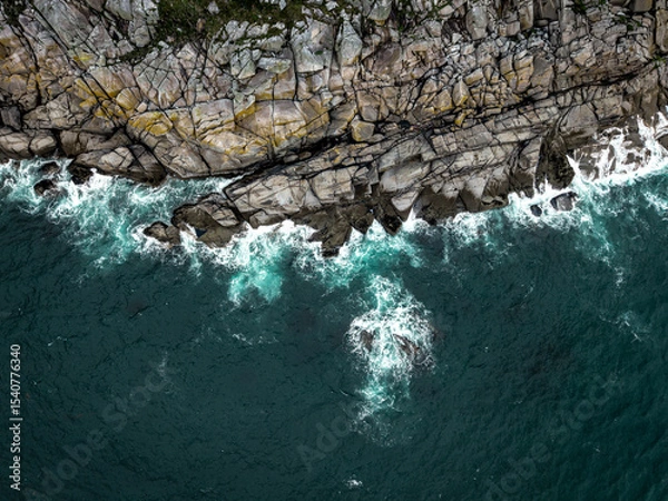 Fototapeta Aerial view directly above steep granite cliffs and rough seas