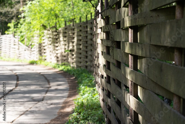 Fototapeta Road in a village with trees and beautiful wodden fence at the right side. Sunny summer day.