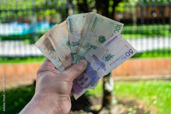 Fototapeta Colombian peso bills held by a man, blurred background outdoors