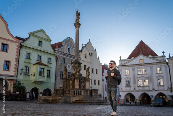 Obraz Hombre turista paseando por el centro de český krumlov, con la fuente y la columna de la peste de fondo