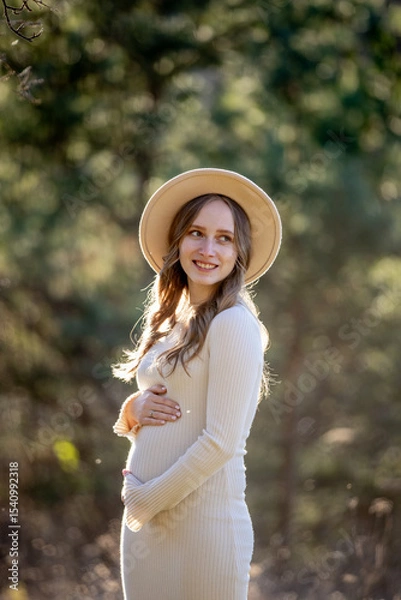 Fototapeta A beautiful pregnant woman is posing gracefully amidst a lush green setting, radiating immense joy and tranquility