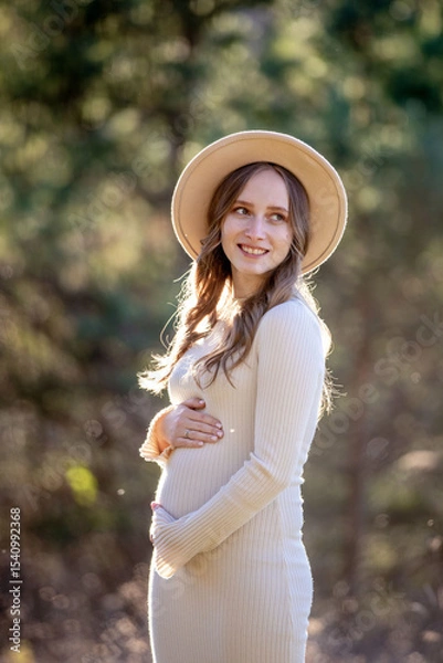 Fototapeta A beautiful pregnant woman is posing gracefully amidst a lush green setting, radiating immense joy and tranquility