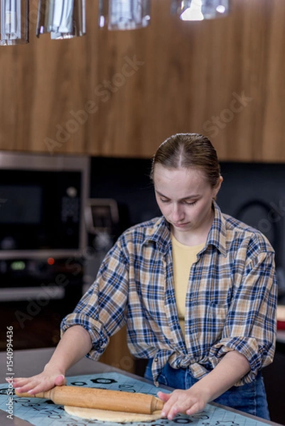 Fototapeta Woman skillfully rolls out dough, perfectly showcasing her culinary expertise in a kitchen