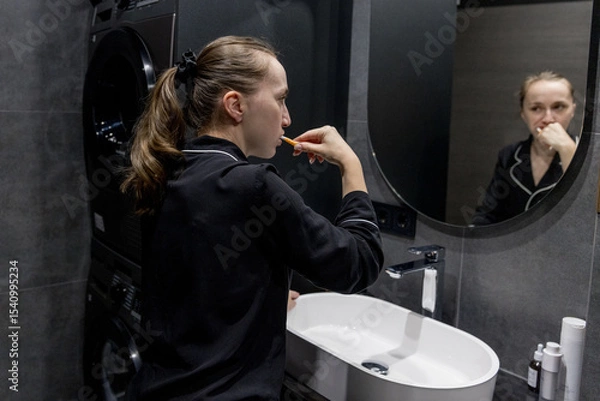 Fototapeta A woman in comfy pajamas brushes her teeth in a modern bathroom, enjoying her daily selfcare routine. Morning Routine