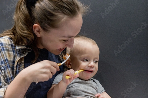 Fototapeta A woman with her baby brushes her teeth while holding a baby in hands in the bathroom