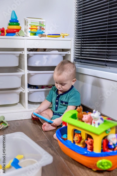 Fototapeta A baby sits on the floor, happily playing with toys