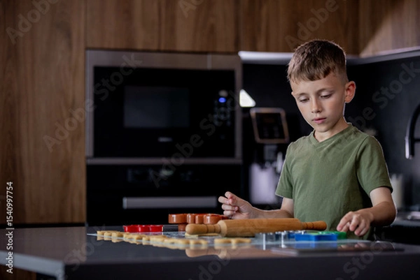 Fototapeta Little boy rolling out gingerbread dough on the table with a rolling pin.