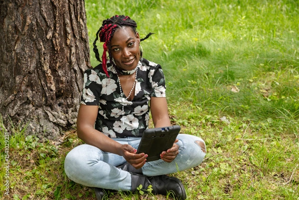 Fototapeta African American Student with Colorful Braids Using Digital Tablet in Park for Learning
