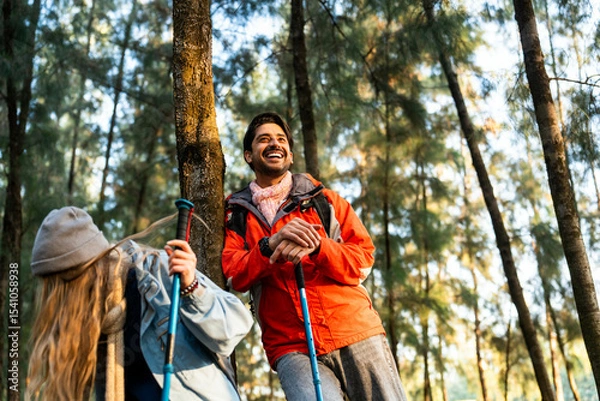 Fototapeta Young Couple Resting Against Tree During a Winter Hike. Enjoying the Golden Hour Light in a Peaceful Forest, Wearing Warm Clothes and Backpacks, Sharing a Quiet and Happy Moment Together