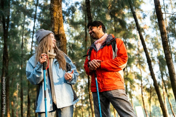 Fototapeta Young Couple Resting Against Tree During a Winter Hike. Enjoying the Golden Hour Light in a Peaceful Forest, Wearing Warm Clothes and Backpacks, Sharing a Quiet and Happy Moment Together