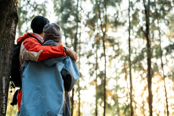 Fototapeta Couple Hugging in Forest at Sunset. Rear View of Romantic Travelers in Warm Winter Clothes Standing Together, Embracing Peacefully While Enjoying the Tranquil Nature and Soft Golden Light