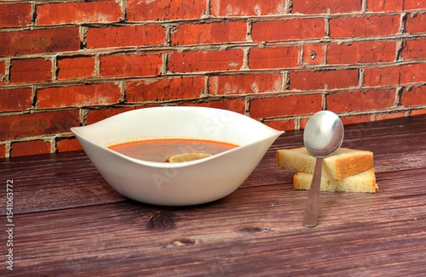 Obraz Solyanka, a tasty Russian soup with a lemon wedge in a deep ceramic bowl on a wooden table, a tablespoon and two pieces of wheat bread nearby.