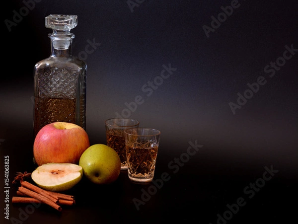 Obraz Apple liqueur in a crystal decanter and two glasses on a black background, next to pieces of ripe fruit and cinnamon with anise.