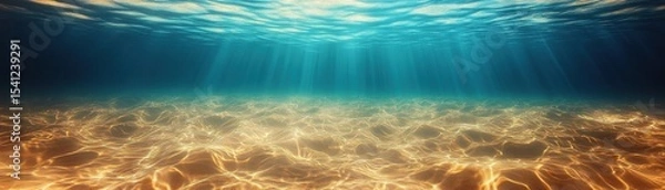 Fototapeta Underwater scene showing sun rays penetrating clear water above a sandy ocean floor with gentle ripples and patterns.