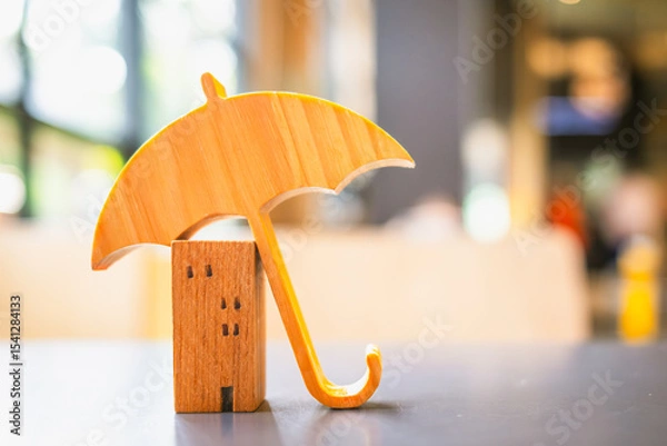 Fototapeta Model of umbrella with house on wooden table concept of the system of insurance savings and Housing insurance against impending loss and fire, building fire insurance concepts.