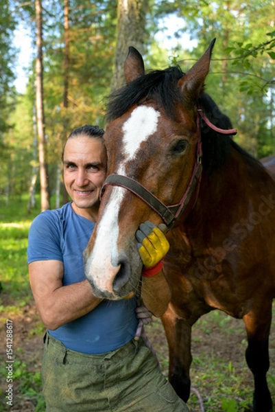 Obraz rustic man with  horse in rural village near  forest.  horse farm is surrounded by nature, hay is stacked nearby,  peaceful and traditional.  man is caring for  horse
