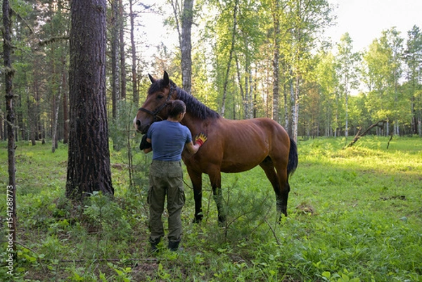 Obraz rustic man with  horse in rural village near  forest.  horse farm is surrounded by nature, hay is stacked nearby,  peaceful and traditional.  man is caring for  horse