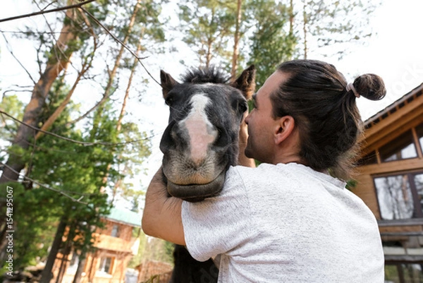 Obraz rustic man with  horse in rural village near  forest.  horse farm is surrounded by nature, hay is stacked nearby,  peaceful and traditional.  man is caring for  horse