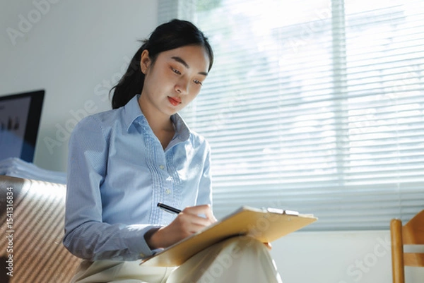 Fototapeta Businesswoman working from home taking notes on clipboard