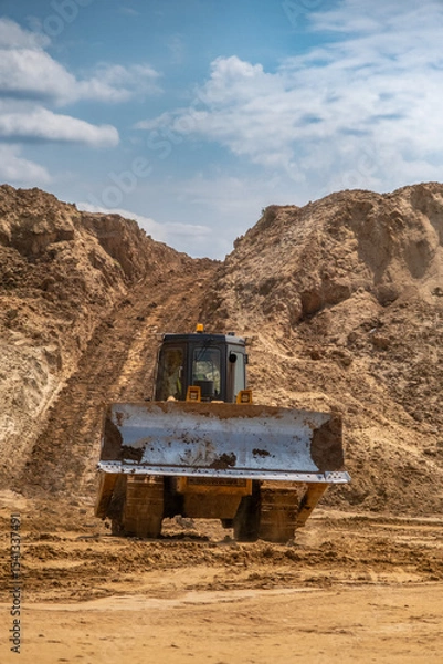 Fototapeta A crawler tractor with a bucket works in a sand quarry.