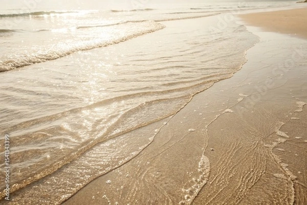 Fototapeta Gentle Ocean Waves Washing Over Sandy Beach. Peaceful shoreline with soft waves lapping against the golden sand, captured in warm sunlight during a calm day at the beach