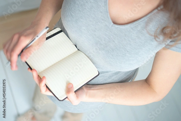 Fototapeta Overhead shot of future mother writing crucial to-do list for maternity period. Detailed organization of hospital bag and birth preparation notes.