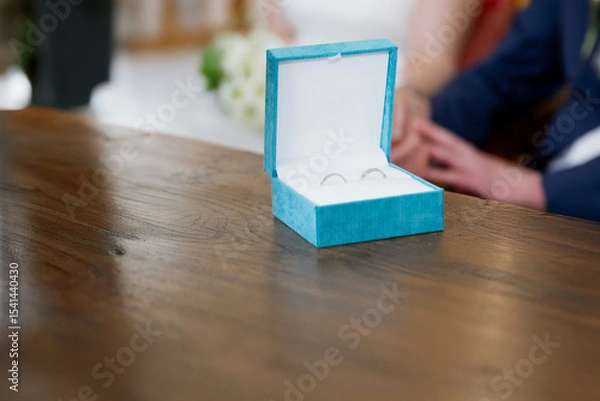 Obraz Close up of a blue box with two silver wedding rings on a wooden table, blurred background 