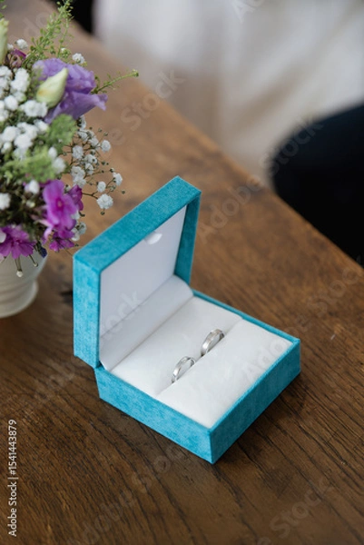 Obraz Close up of a blue box with two silver wedding rings on a wooden table, blurred background 