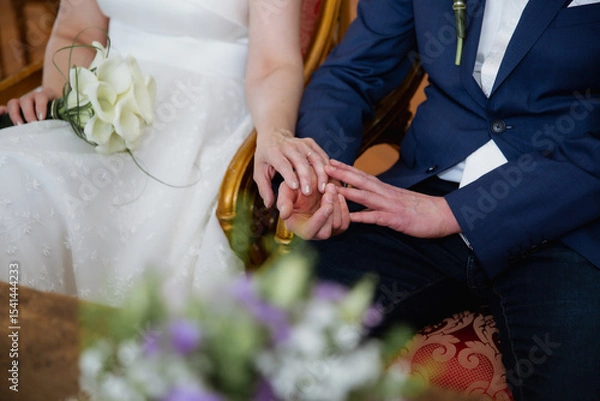 Obraz Close up of bride and groom holding hands sitting together, wedding day concept