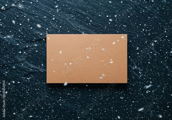 Fototapeta Blank kraft paper card mockup on dark wooden surface with falling snow