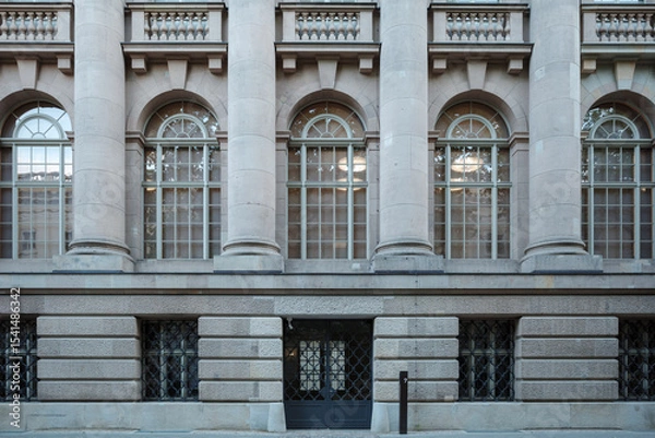 Fototapeta A detailed view of a classical stone building facade featuring large arched windows on the upper level, framed by imposing columns.
