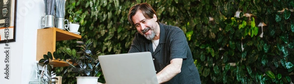 Fototapeta Cheerful cafe owner chats with a financial advisor via video call at his cozy coffee shop. Surrounded by greenery, he discusses business strategies and growth opportunities with enthusiasm.