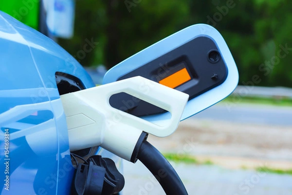 Obraz Close-up of an electric charger connected to a blue electric vehicle. Clean energy concept and the transition to green transportation.