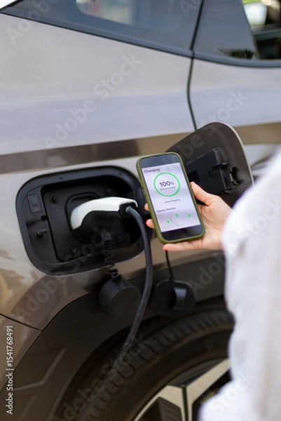 Obraz Businesswoman using smartphone app while charging electric car at public station