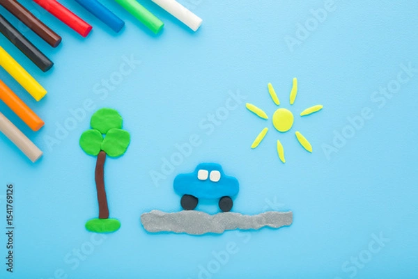 Fototapeta Created car, road, tree and sun from colorful modeling clay on light blue table background. Pastel color. Closeup. Top down view.
