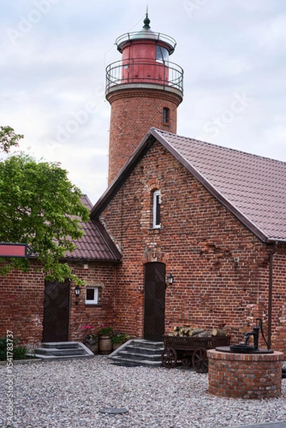 Obraz A beautifully picturesque brick lighthouse situated right next to a charming rustic home, all set against a cloudy sky