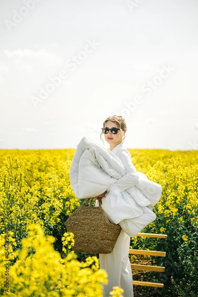 Fototapeta Woman carrying a blanket in a bright yellow flower field during a sunny day